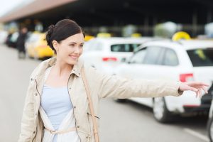 travel, business trip, people, gesture and tourism concept - smiling young woman waving hand and catching taxi at airport terminal or railway station